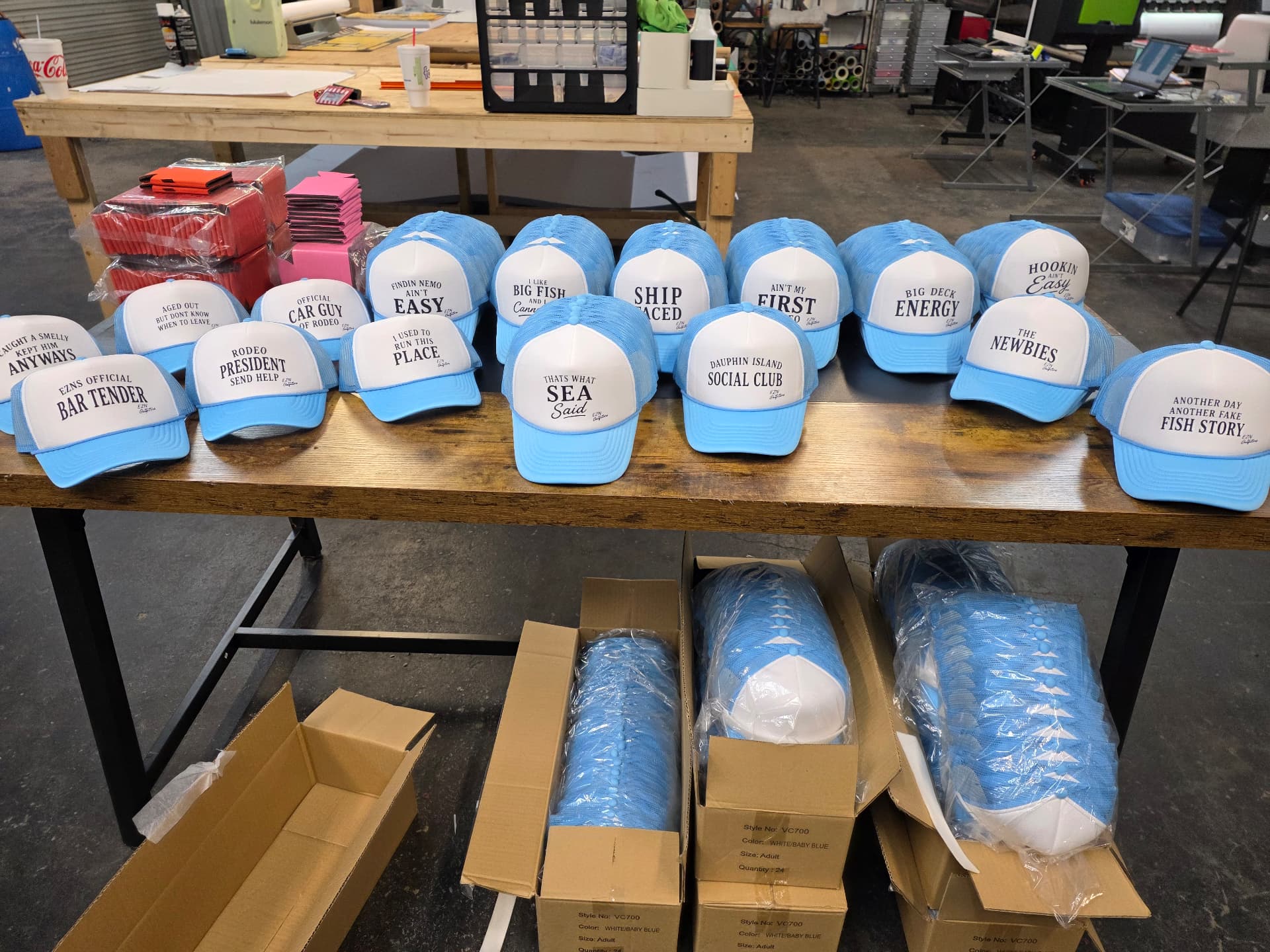 Table of light blue and white trucker hats with custom coastal sayings printed on the front