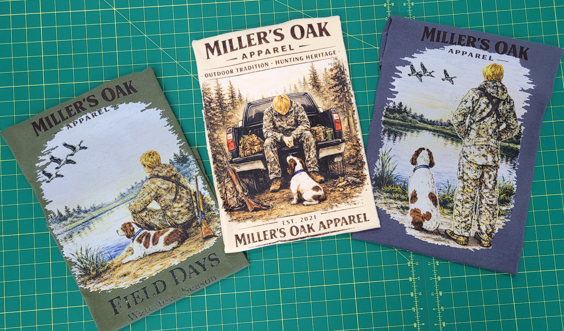 Three custom screen-printed Miller's Oak Apparel shirts with detailed outdoor graphics on a production cutting mat