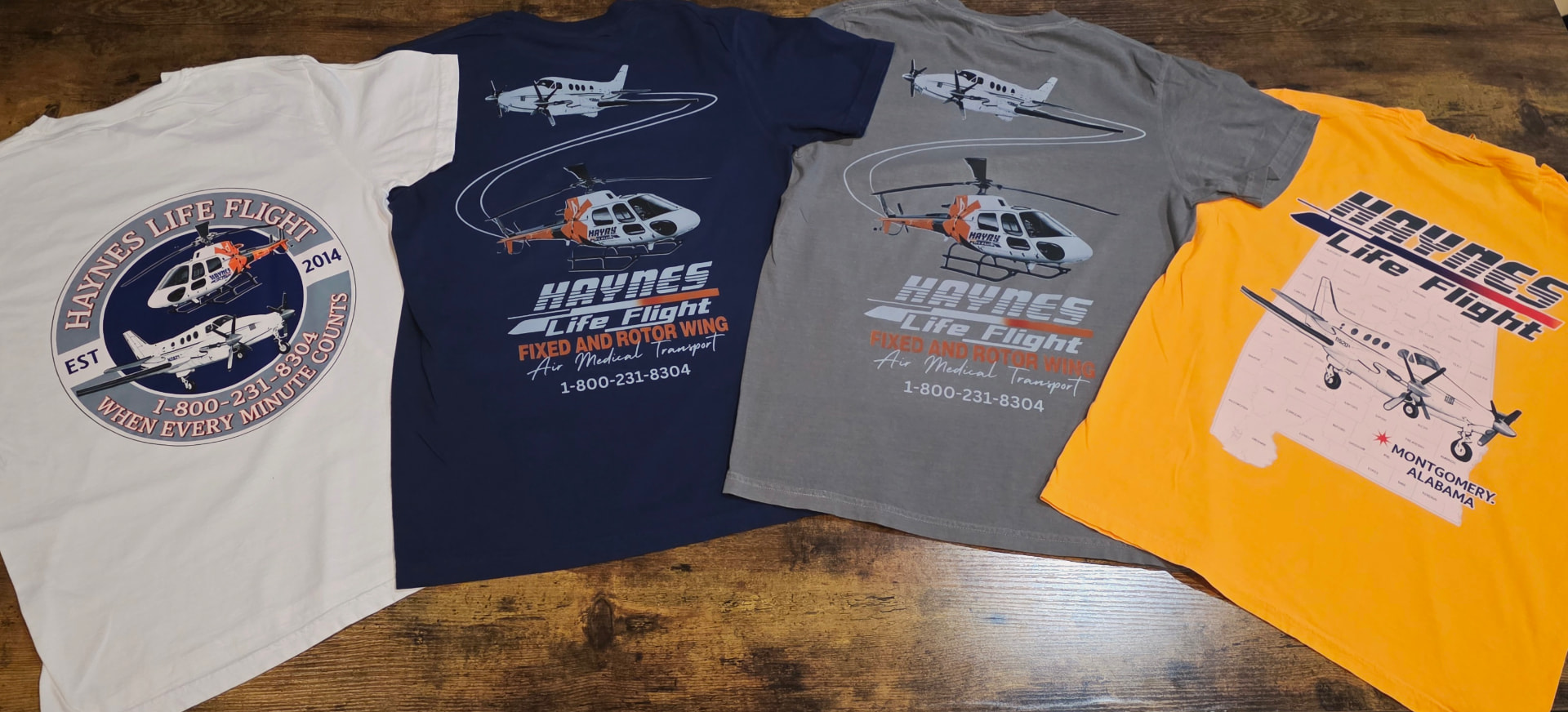 Four Haynes Life Flight t shirts in white, navy, grey, and gold laid out on a workbench